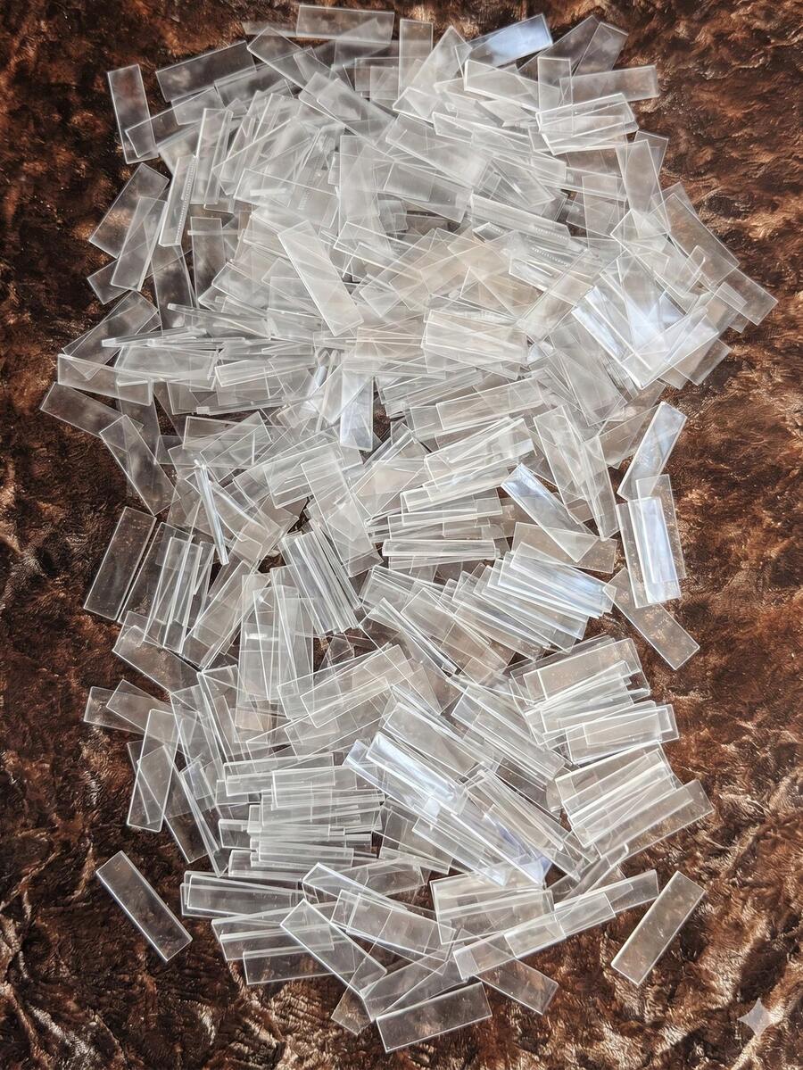 Large pile of clear rectangular fire starter sticks scattered and overlapping on a dark brown textured surface