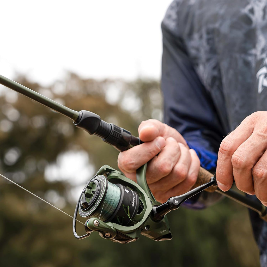 Close-up of hands holding a green fishing rod and a green Spartacus II 3000 spinning reel with teal line on spool