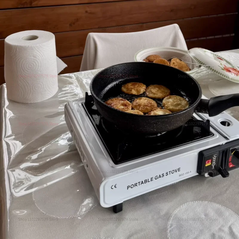 White portable gas stove with a black pan frying food on a table with a clear plastic tablecloth. PORTABLE GAS STOVE BDZ-155-A